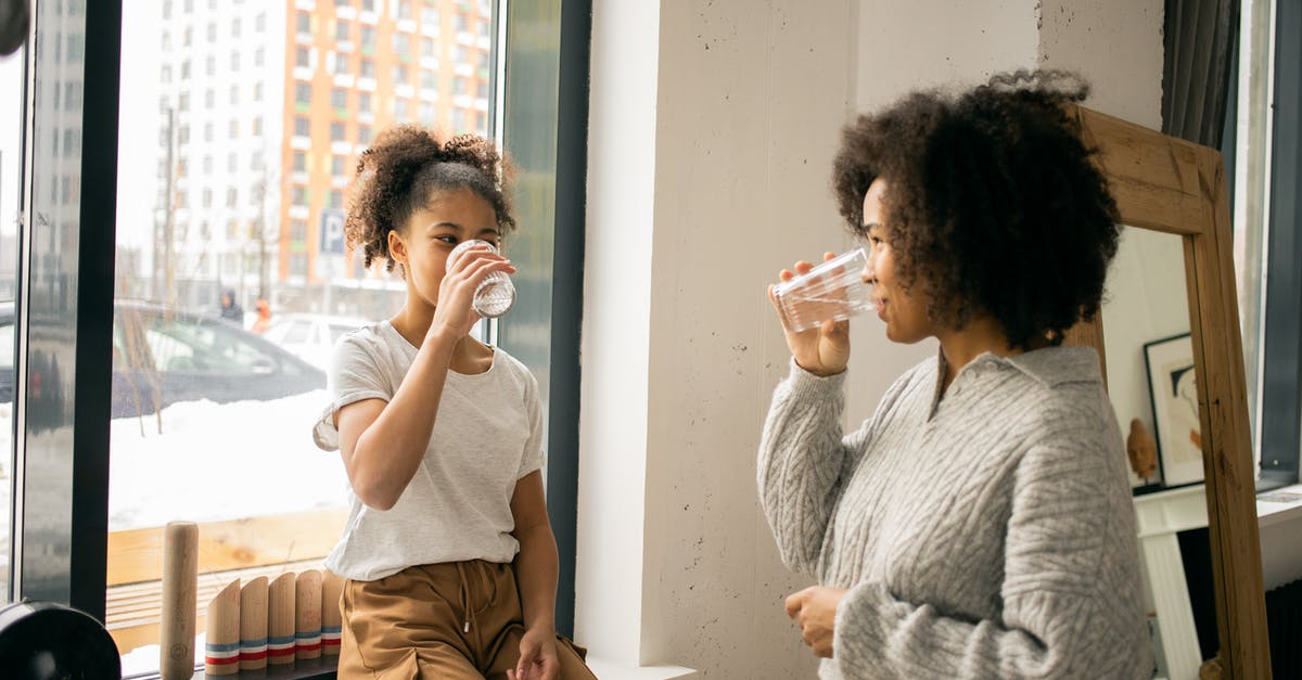 Why did the Arikara spare Glass? - Positive African American mother with daughter in casual wear looking at each other while drinking water from glasses in light room
