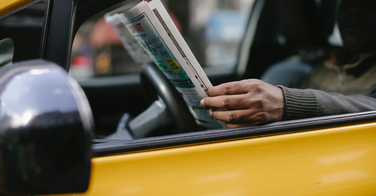 Why did they wait until after the report? - Side view of crop anonymous ethnc male driver reading information in newspaper article while waiting for client