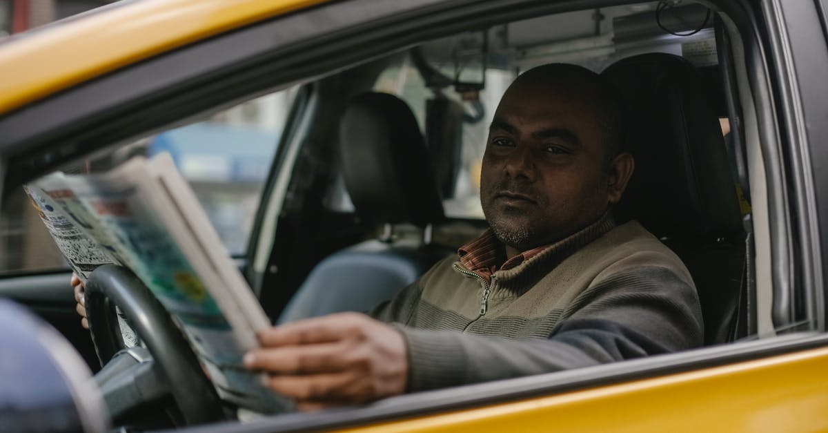 Why did they wait until after the report? - Concentrated ethnic male driver sitting at steering wheel and reading magazine while waiting for client