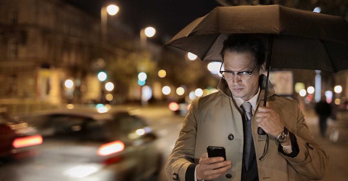 Why did Umbrella never use Nemesis to kill zombies? - Focused formally dressed man in trench holding umbrella while standing on city street and sending message on smartphone