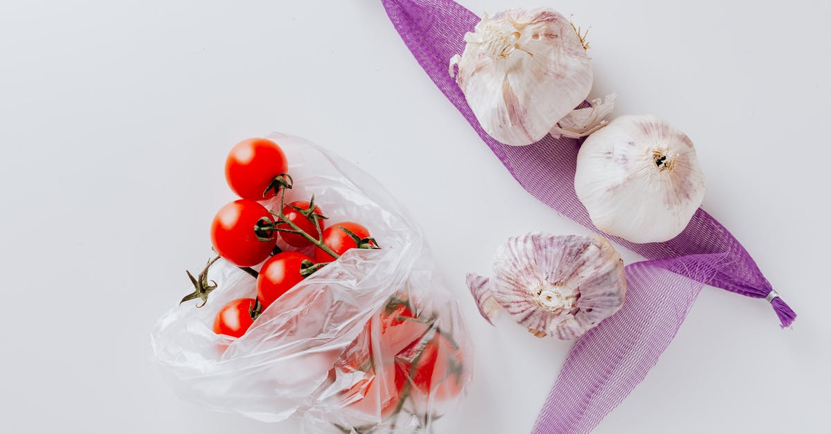 Why did Venom only eat heads? - Top view of fresh cherry tomatoes in transparent polyethylene bag and three heads of garlic placed on purple grid isolated on white background