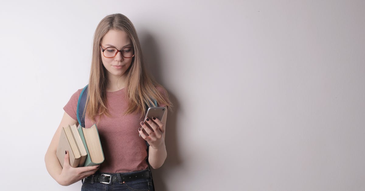 Why didn't Ego take her to his planet? - Confident intelligent female student in eyeglasses wearing pink t shirt and black jeans using cellphone while taking books standing against gray wall