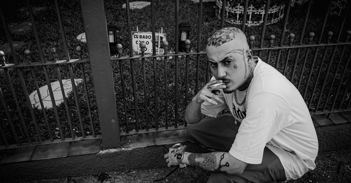 Why didn't Lou hide from the gangster in the climax of "Nightcrawler"? - Black and white from above of serious tattooed male smoking cigarette while sitting on haunches near metal fence on street