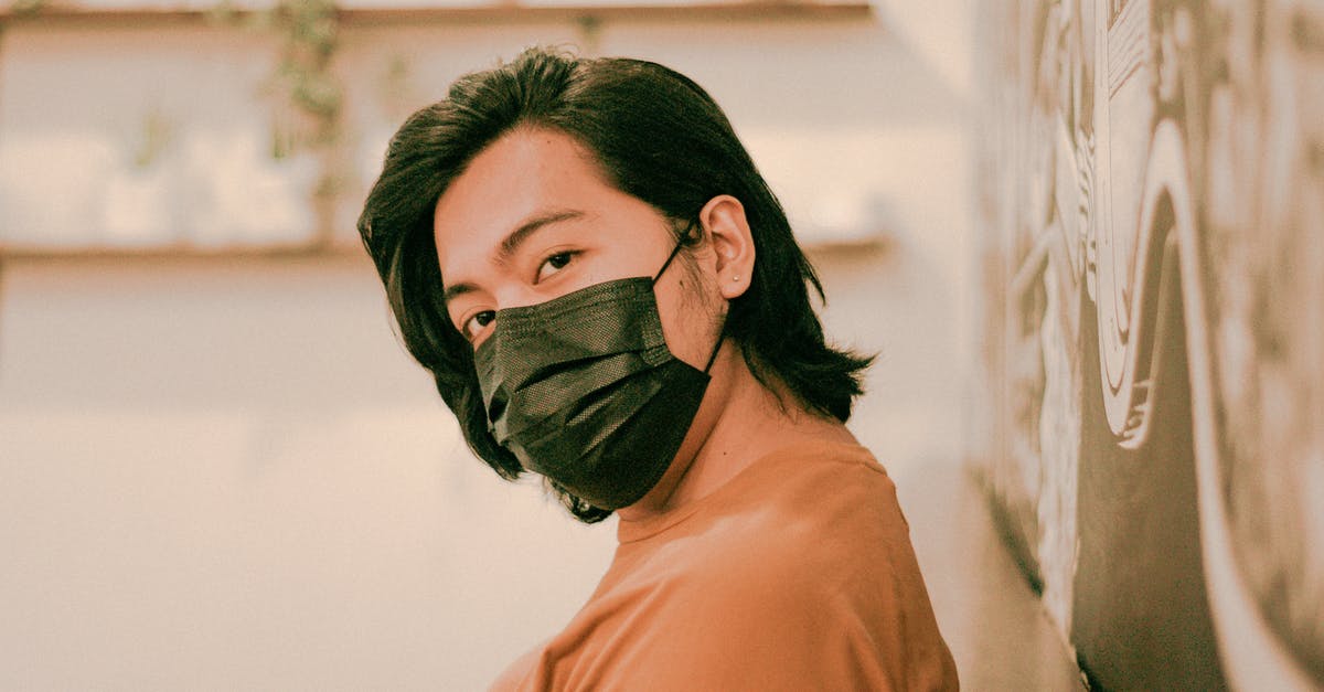 Why didn't Oliver wear the mask? - Pensive Asian male in black protective mask looking away while sitting near wall in modern cafeteria on blurred background during pandemic