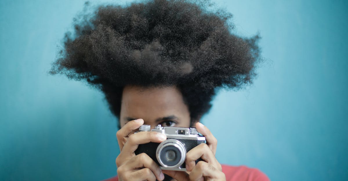 Why didn't "Dutch" & his commandos bring any thermal imaging devices? - Ethnic male with creative Afro hairstyle wearing pink t shirt taking pictures on retro photo camera against blue background while looking at camera