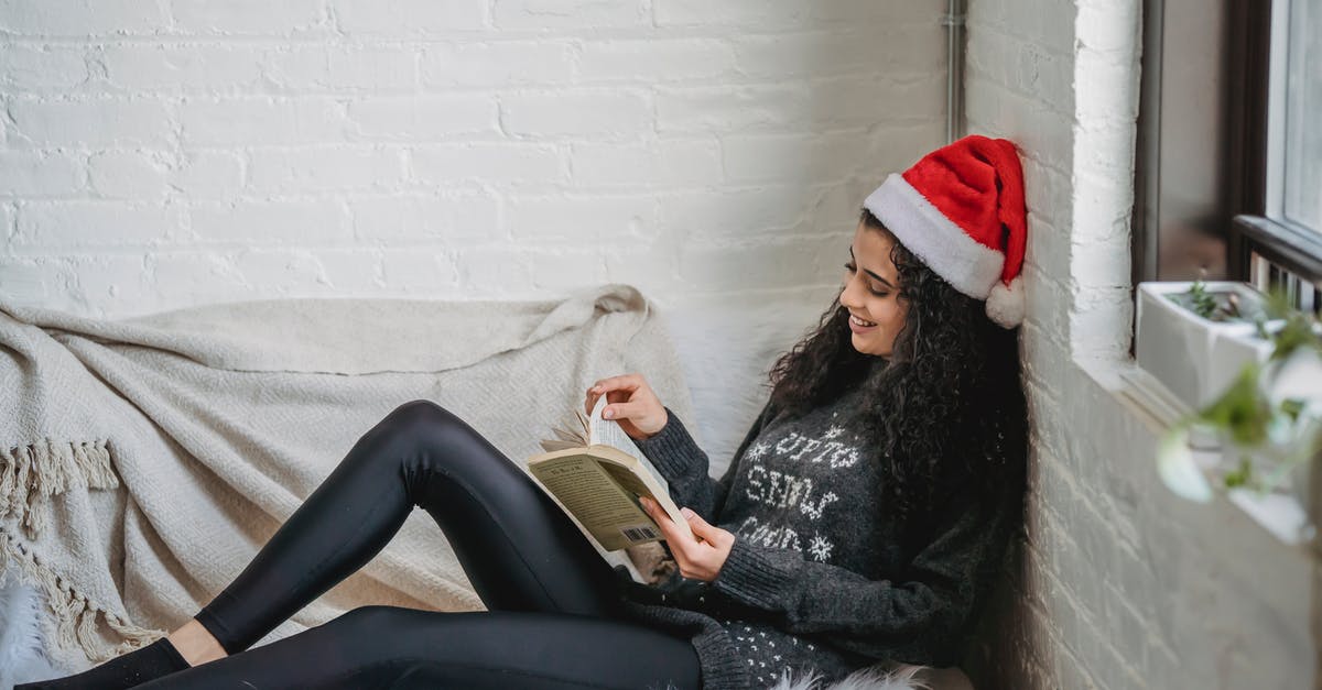 Why do Adam and Eve live so far apart? - Side view of young female in casual clothes and Santa hat resting on sofa and reading book in modern living room on Christmas