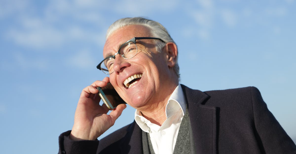 Why do people repeatedly hit the phone hook switch when disconnected? - From below of delighted aged male entrepreneur in classy outfit standing on street and speaking on cellphone while laughing and looking away