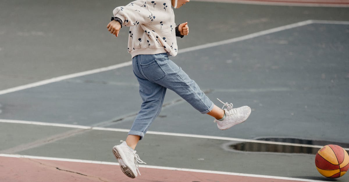 Why do the kicks have to occur simultaneously? - Side view of jumping little girl in jeans and jumper kicking colorful ball playing on sports yard
