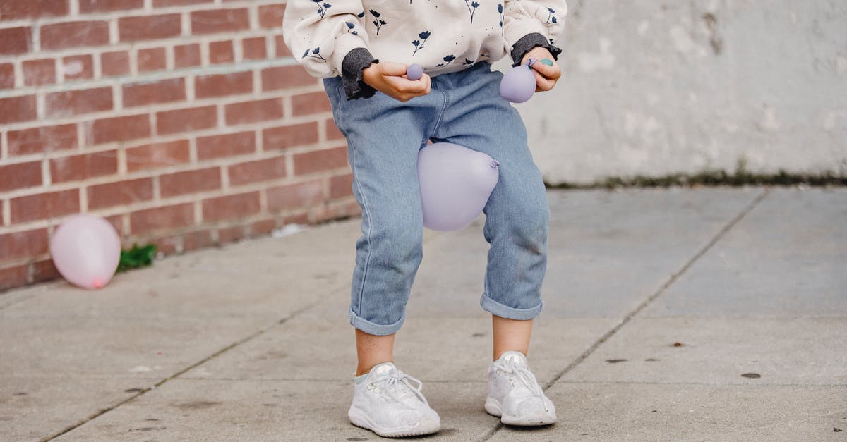 Why do the kids have different accents? - Crop anonymous kid in trendy wear playing with balloon between legs while standing on tiled pavement in town