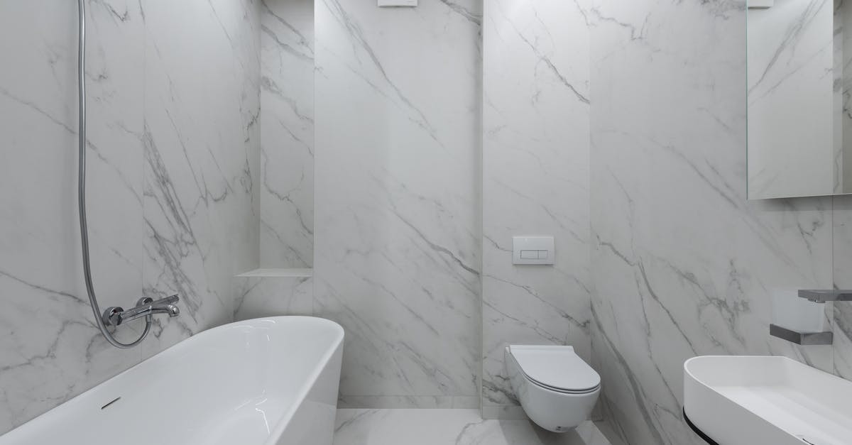 Why do they go to the toilet and put the hose in it to breathe? - Interior of stylish bathroom with marble walls and bath placed near toilet and ceramic sink in light room with mirror