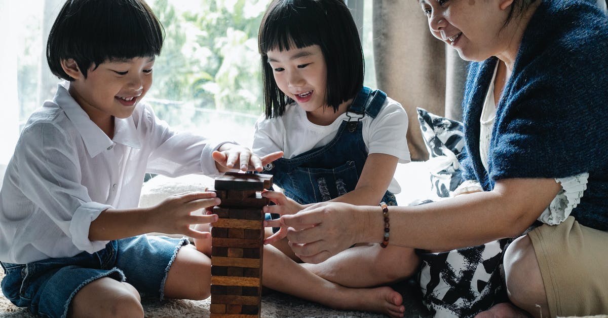 Why do they have to be barefoot? - Full body of happy ethnic little children with elderly grandmother sitting on floor and constructing wooden tower while playing board game at home