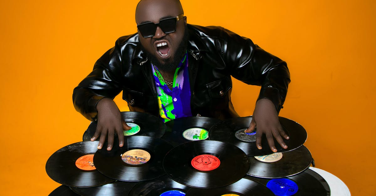 Why does America's Got Talent have so many executive producers? - Skilled African American male DJ in leather jacket standing in studio while scratching abundance of various vinyl records on orange background