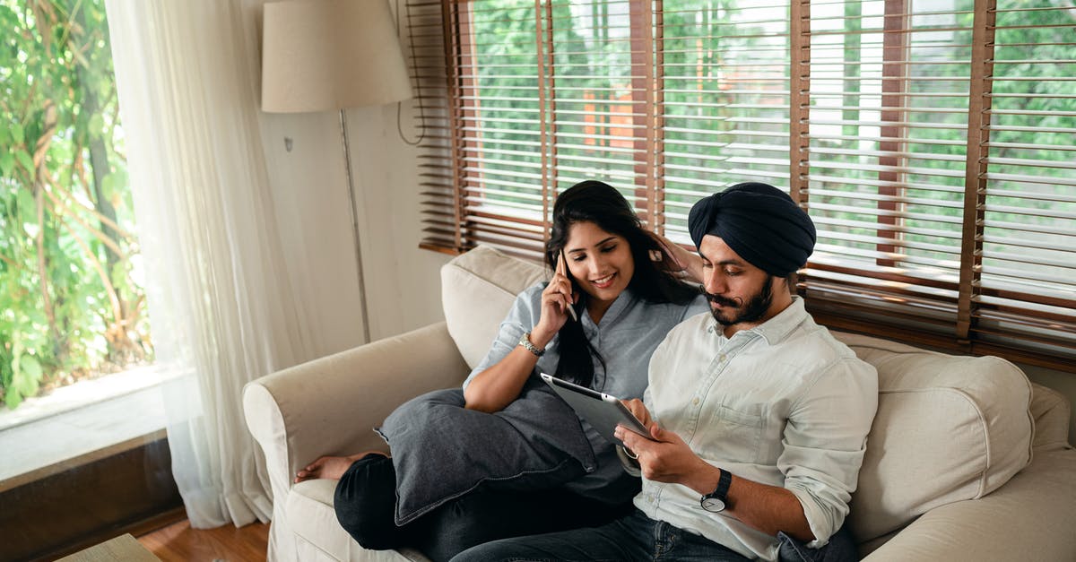 Why does Brody's wife call him by his surname? - Young Indian man browsing tablet while woman talking on smartphone on couch