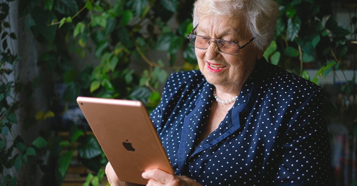 Why does Cassius Green speak like this? - Aged cheerful female smiling and using contemporary tablet while talking on tablet in living room with green plant