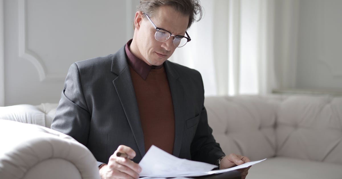 Why does Dormer hesitate to sign Ellie's report? - Elegant adult man in jacket and glasses looking through documents while sitting on white sofa in luxury room