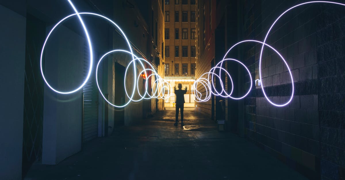 Why does Maria flee the flashlight beam? - Long exposure full body person silhouette making circles with bright flashlight while standing on narrow dark city street between tall urban buildings