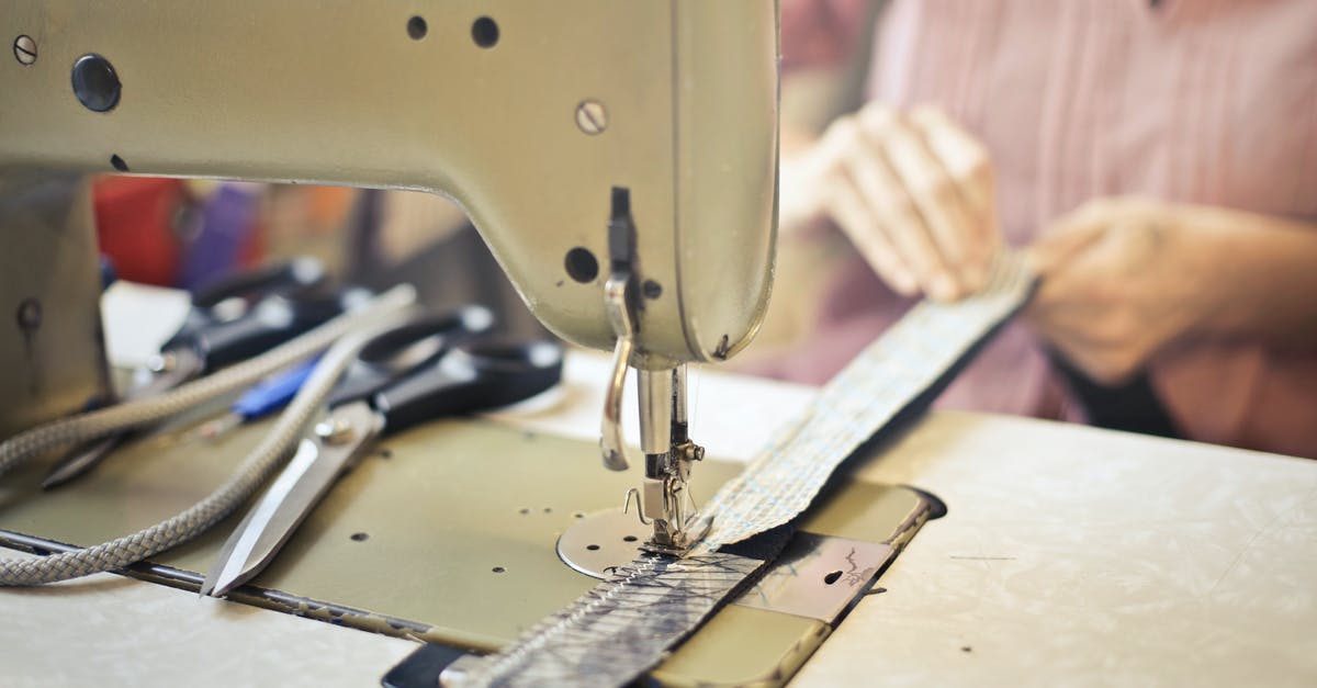 Why does Master Ip want to sew a button onto a paper? - Crop craftswoman in casual wear sitting at old fashioned sewing machine and stitching pieces of fabric while working in workshop
