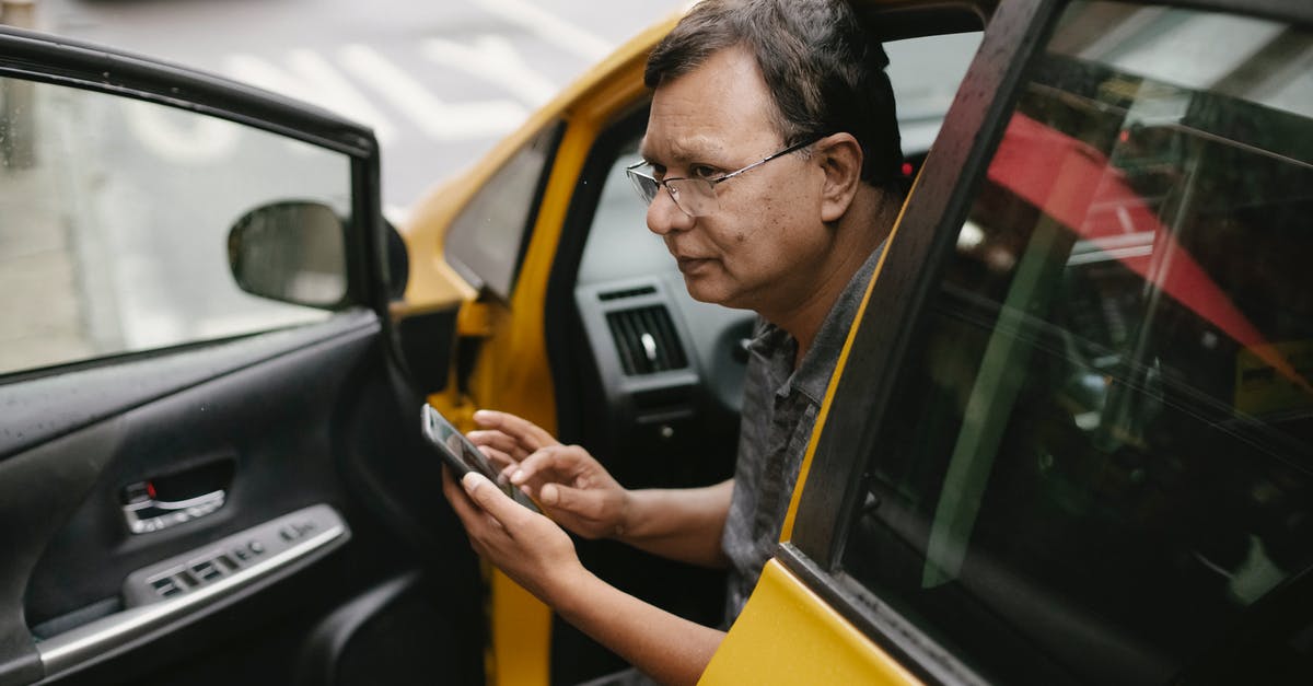 Why does not Sheldon use Taxi Cabs for his Transport issues? - Crop Asian man sitting in parked yellow taxi car with open door and using smartphone while looking away