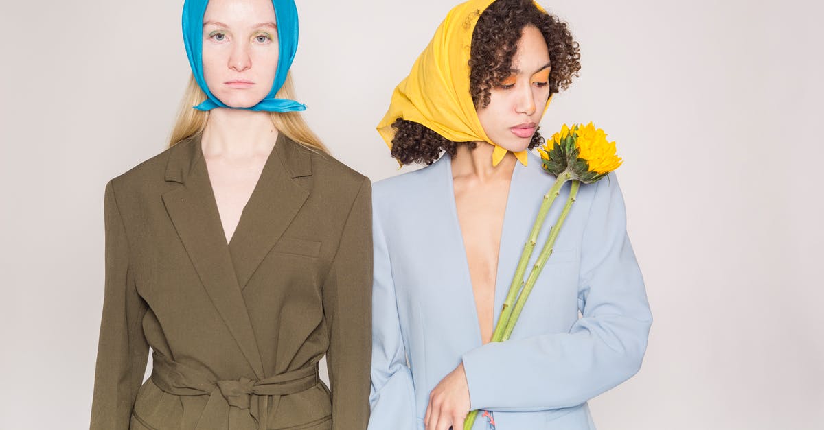 Why does Sophie wear the jacket inside out? - Charming ethnic woman with curly hair in stylish clothes standing with sunflower near serious female with blond hair against beige background in studio