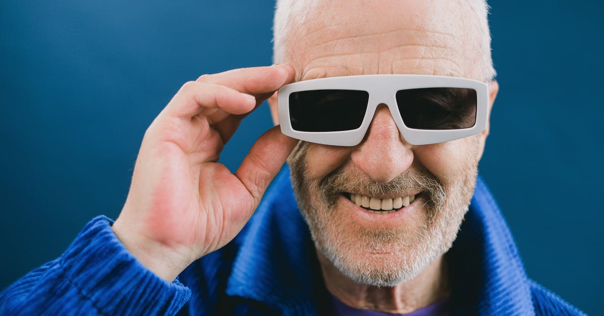 Why does Sophie wear the jacket inside out? - Portrait of smiling elderly unshaven male with gray hair wearing blue jacket and sunglasses looking at camera against blue background