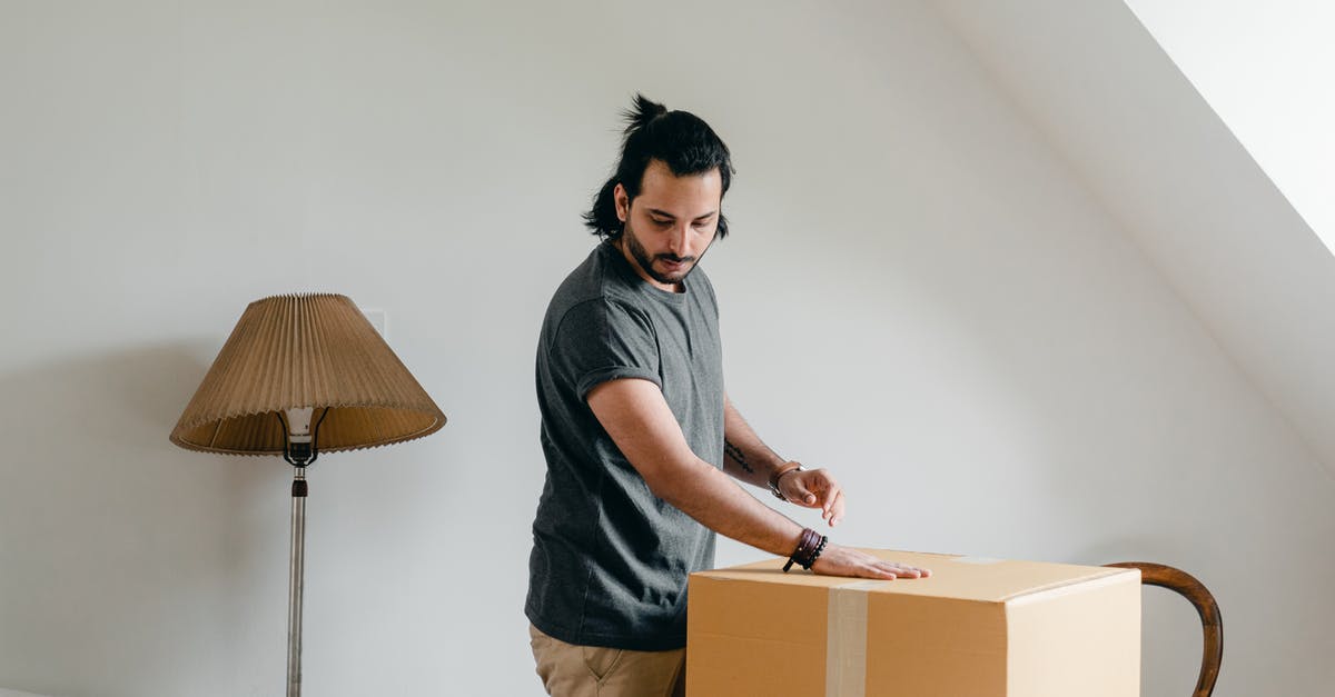 Why does the chair move by itself? - Side view of fit pensive ethnic male in casual wear and wristwatch putting palm of hand onto cardboard box and looking down in attic style apartment
