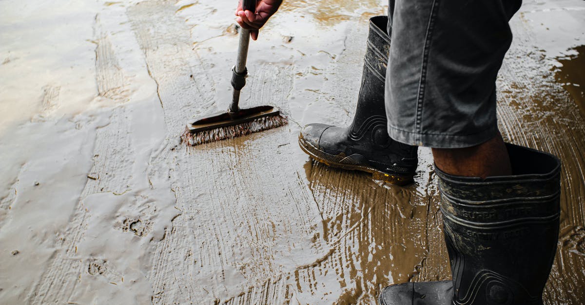 Why does the prime minister "redistribute" Natalie? - Side view of crop anonymous male worker in gumboots with brush priming cement floor at work
