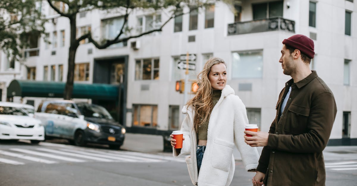Why does the talking zebra always address Candace as Kevin? - Stylish young guy and lady in trendy outfits holding hands and drinking coffee to go while crossing road in city on autumn day