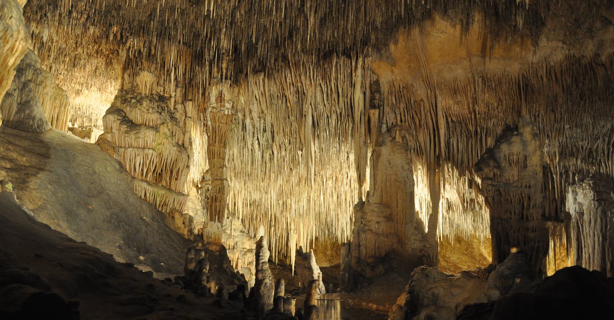 Why does the water hang from the ceiling in an underground cave? - Brown Stalactites Hanging on Cave Ceiling