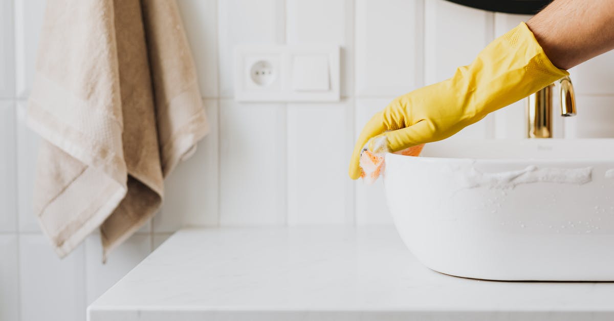 Why does Tyrell Wellick put on latex gloves in Elliot's apartment? - Crop anonymous person wearing yellow latex gloves washing sink in bathroom with orange sponge and cleanser while cleaning contemporary flat