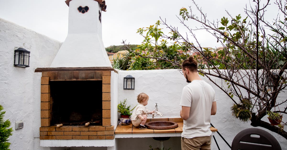 Why doesn't Eames impersonate Robert Fischer's father to plant the idea in his mind? - Man wearing casual clothes exploring outdoor kitchen with fireplace and sink together with cute toddler kid in backyard near white stone fence during daytime at countryside