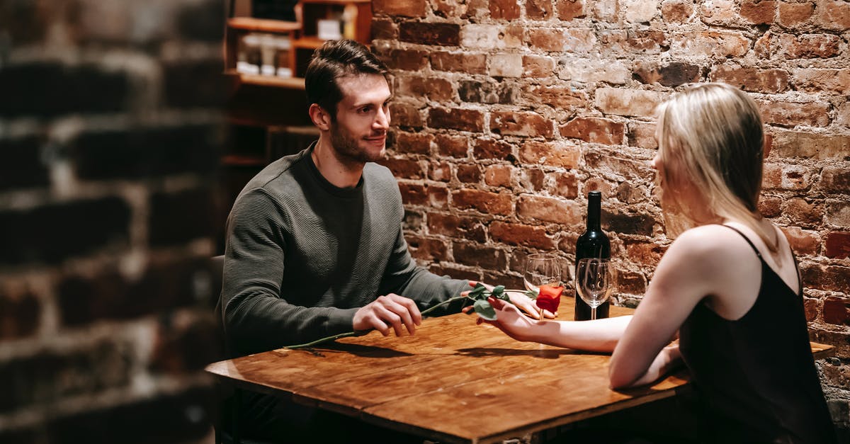 Why doesn't Vesper give Bond the additional $5M? - Loving boyfriend giving red rose to girlfriend while sitting near brick wall at wooden table during celebration of event in restaurant