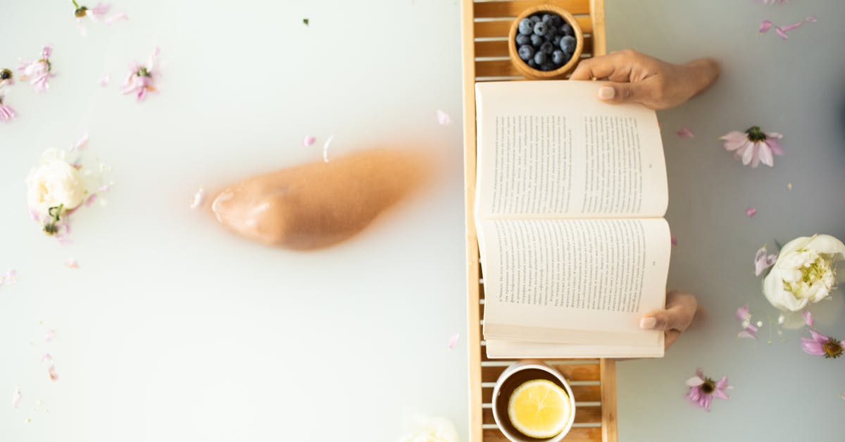 Why female academy bathrooms so visible from outside? - Top view of crop unrecognizable lady in white water in bathtub with fresh colorful flower petals with wooden tray with cup of tea with lemon and blueberries while reading book