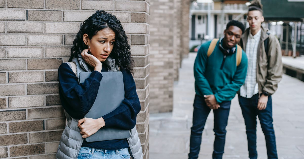 Why hide the relationship from Tom? - Latin American woman leaning on brick wall while hiding from multiracial classmates in college
