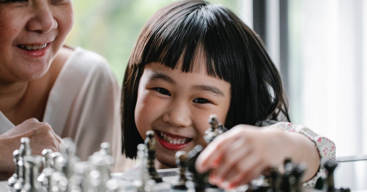 Why is Game of Thrones aimed at such a mature audience? - Cheerful woman sitting near little granddaughter and smiling while playing chess at home