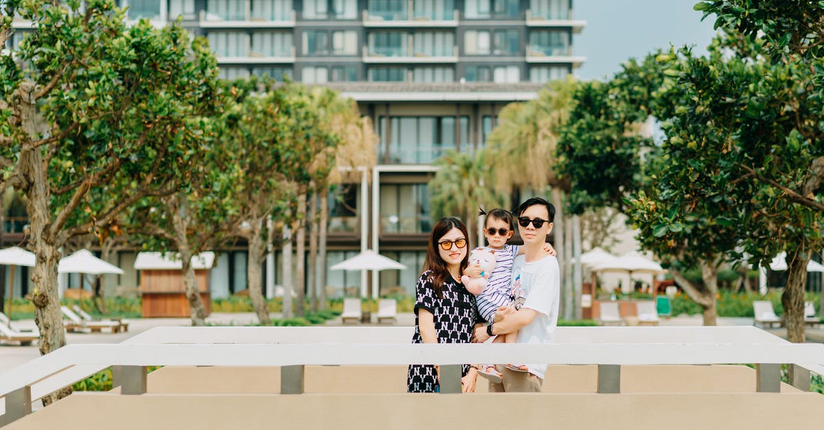 Why is Leslie's mom cool with Parker? - Positive young Asian couple with child wearing casual clothing and stylish sunglasses while standing among green tropical trees and looking at camera