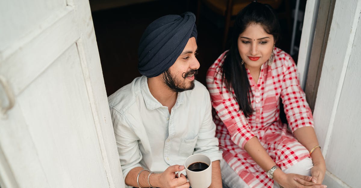 Why is Ranajay unable to tell Iman that he loves her? - From above of good looking Indian wife listening to husband sharing news with cup of coffee in hand while both sitting at doorstep of house