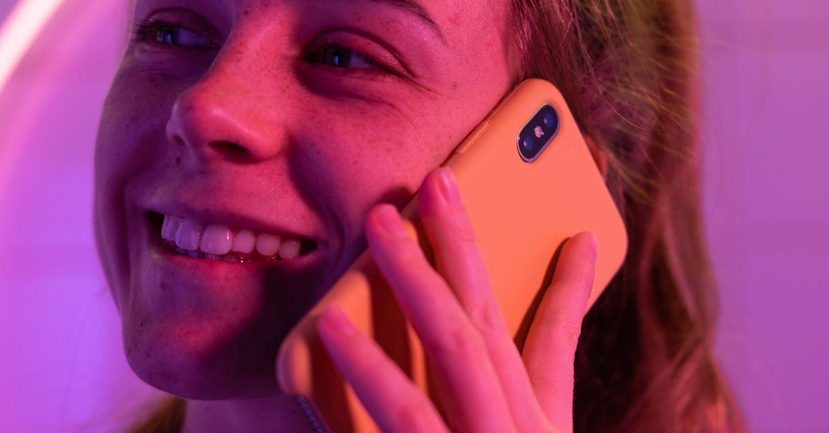 Why is the purple wedding called purple wedding? - Crop happy female smiling and speaking on mobile phone while looking away in ultraviolet light on blurred background