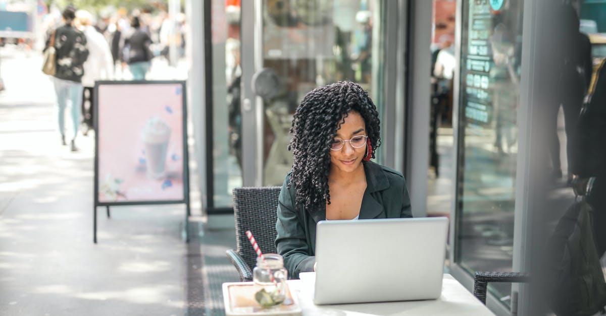 Why not just use fingerprint identification? - High angle of pensive African American female freelancer in glasses and casual clothes focusing on screen and interacting with netbook while sitting at table with glass of yummy drink on cafe terrace in sunny day