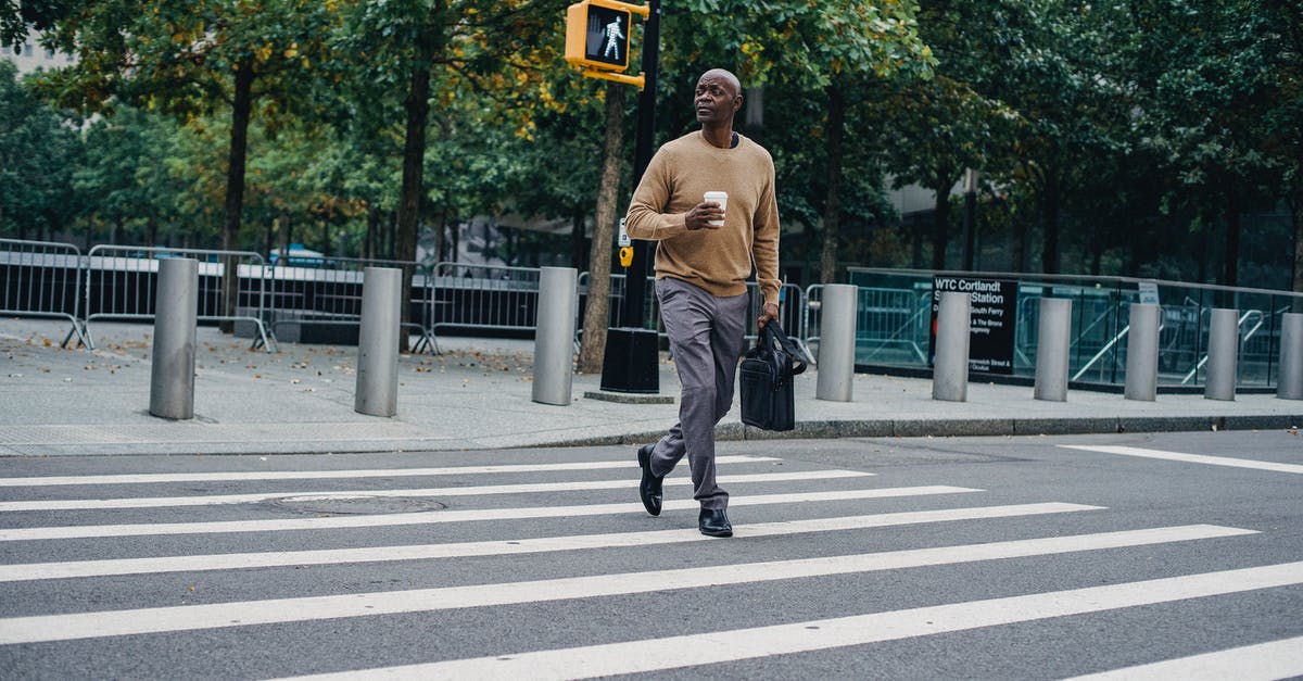 Why the empty briefcase? - Full body of African American male walking on pedestrian crossing on asphalt road with cup of hot drink and briefcase
