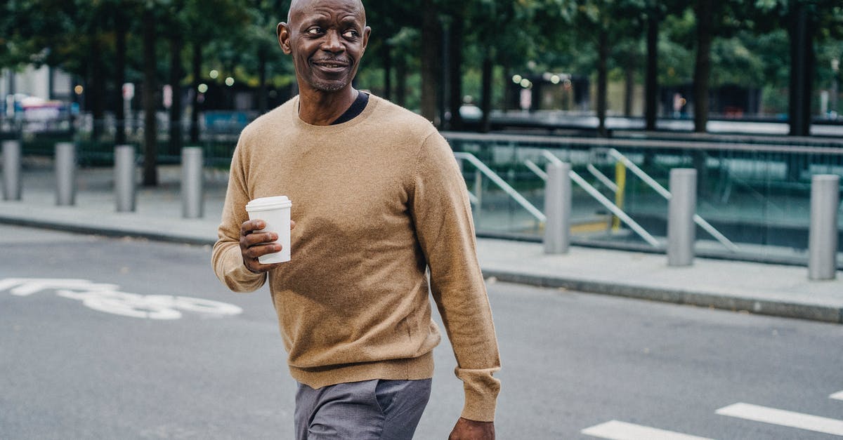 Why the empty briefcase? - Cheerful middle aged African American male with cup of hot drink and briefcase walking on pedestrian crossing on street while looking away