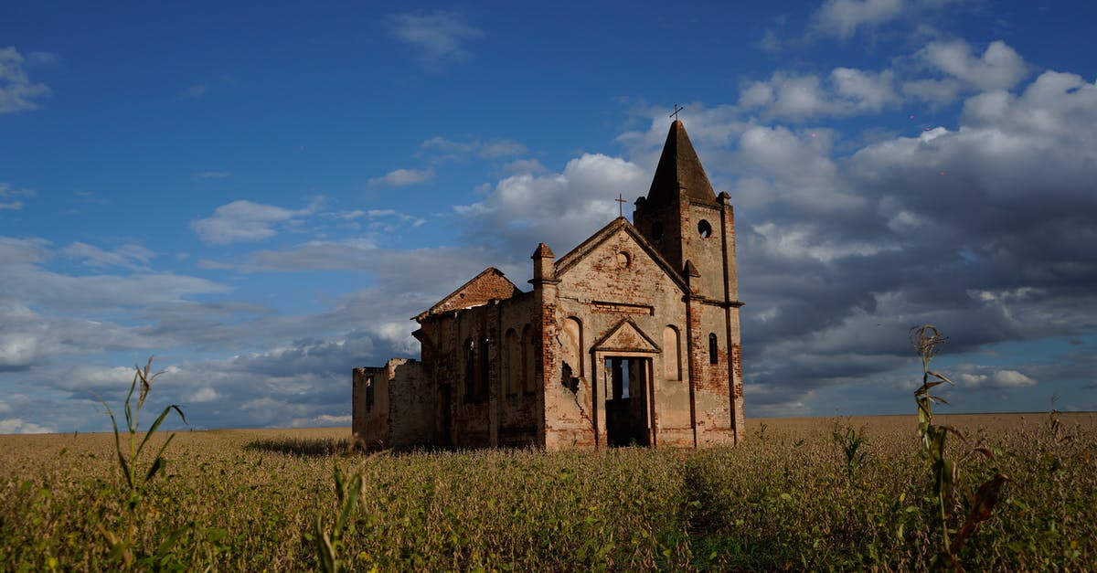 Why was Evey out past curfew in the first place? - Exterior of ruined medieval church with remaining masonry walls and crosses on top located on spacious grassy valley