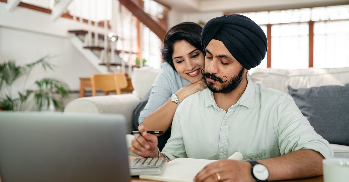 Why was The Accountant feeding information to King? - Cheerful young Indian woman cuddling and supporting serious husband working at home with laptop and counting on calculator