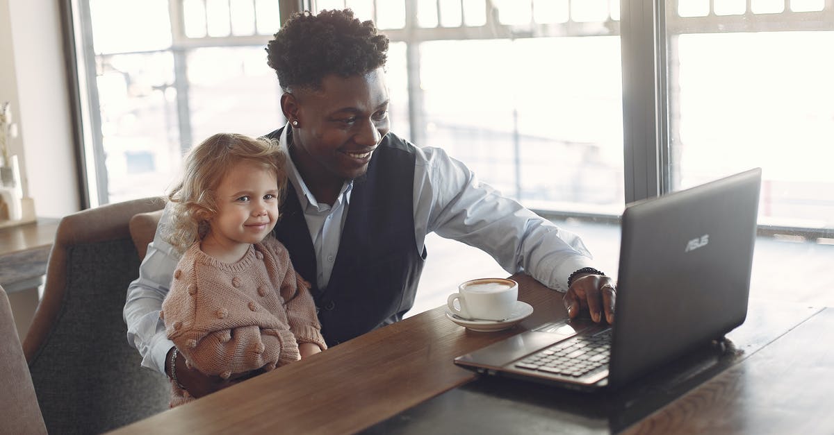 Why was the demon after the little girl? - Cheerful black man in formal wear sitting together with cute child of diverse colleague at table with cup of coffee and using laptop in modern cafeteria during daytime