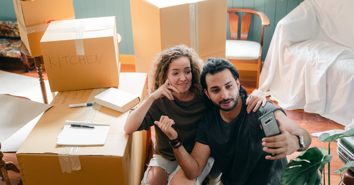 Why was the show The Mentalist moved from Sacramento to Austin? - Top view of trendy woman embracing ethnic boyfriend in casual wear while taking selfie on cellphone and sitting surrounded by heap of cardboard boxes near sofa covered with bed sheet