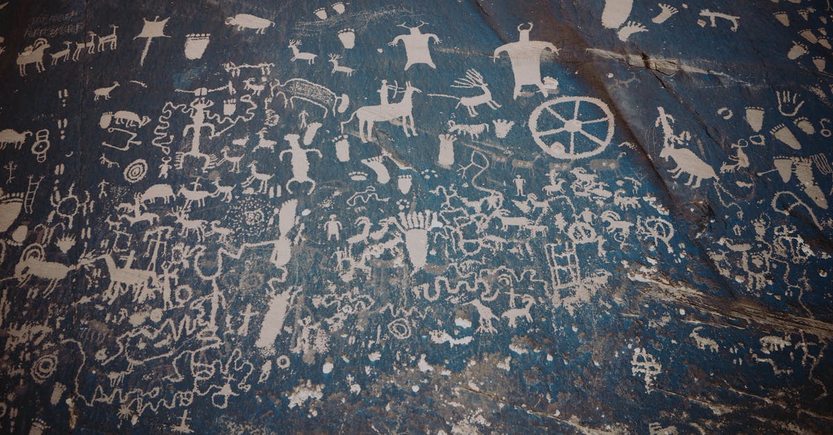 Why was this sailor painting a Swastika on a US Destroyer? - Newspaper rock with ancient symbols and petroglyphs with white paint on shabby stone blue wall with uneven surface in national park