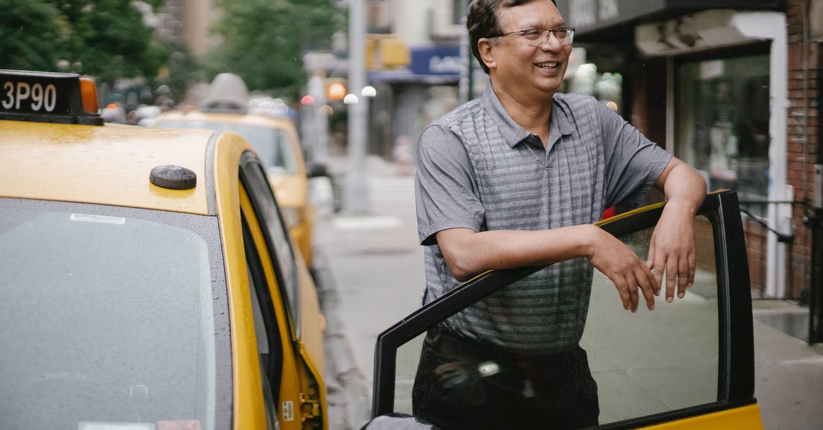 Why wasn't District 12 punished during the 75th Reaping? - Happy man with glasses smiling and standing near yellow taxi on street in city in daytime