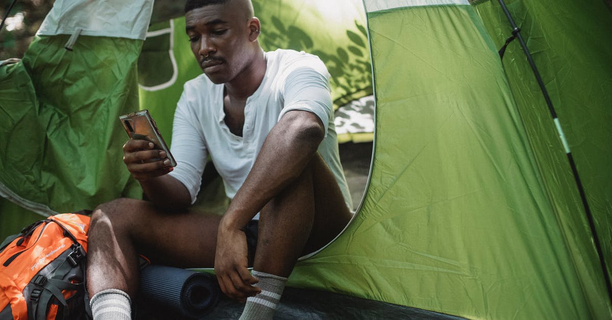 Why were the addicts periodically taken by the "bad guys" to the camp in the desert? - Sad African American male traveler resting in tent and browsing Internet on cellphone while spending journey in nature
