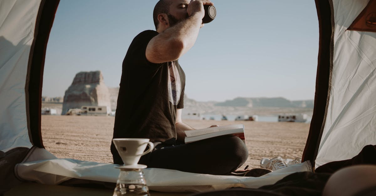 Why were the addicts periodically taken by the "bad guys" to the camp in the desert? - Side view of male traveler sitting in tent with book near pour over cup while drinking hot beverage in nature during trip