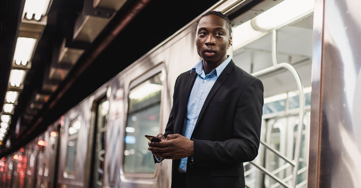 Why would an advanced alien use a subway train to get into the city? - Serious African American man in office wear with mobile phone in hands getting off underground train