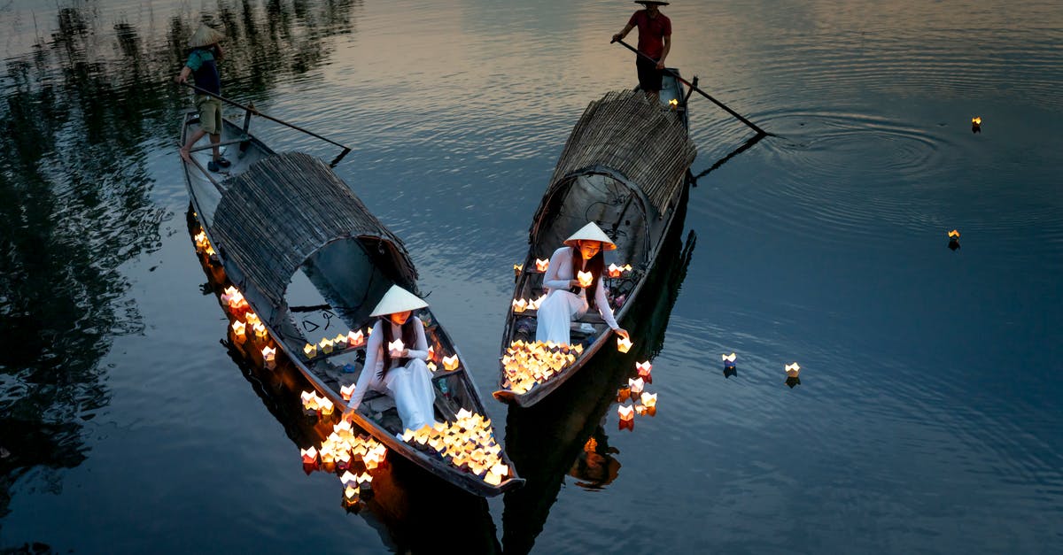 Why would "the stranger" continuously dress the same way? - From above of ethnic female in dresses putting candle lanterns on lake water against anonymous male with oars in boats in twilight